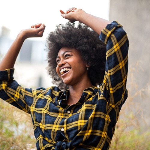Woman smiling outside while dancing in plaid shirt