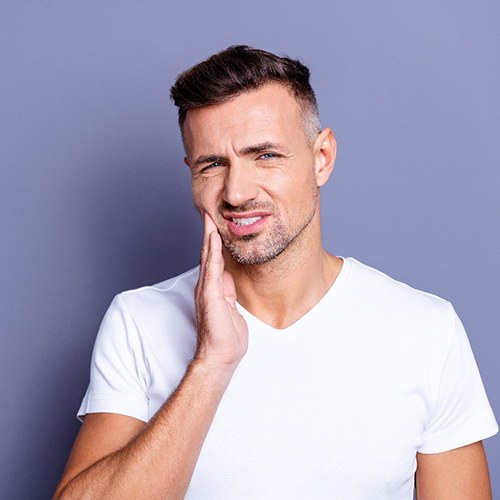 Man in white t-shirt with hand on his face who needs an emergency dentist