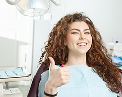 young woman with curly hair sitting in the dental chair and giving a thumbs up 
